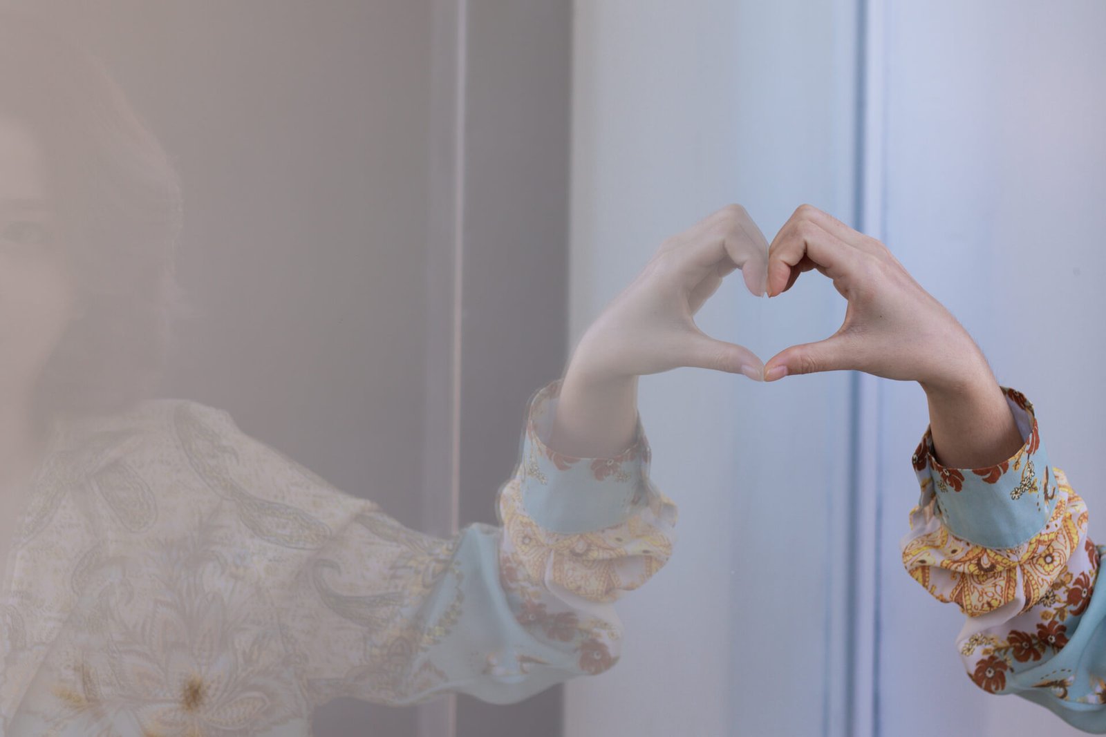 moteris laiko ranką širdelės formoj prie stiklo atspindžio